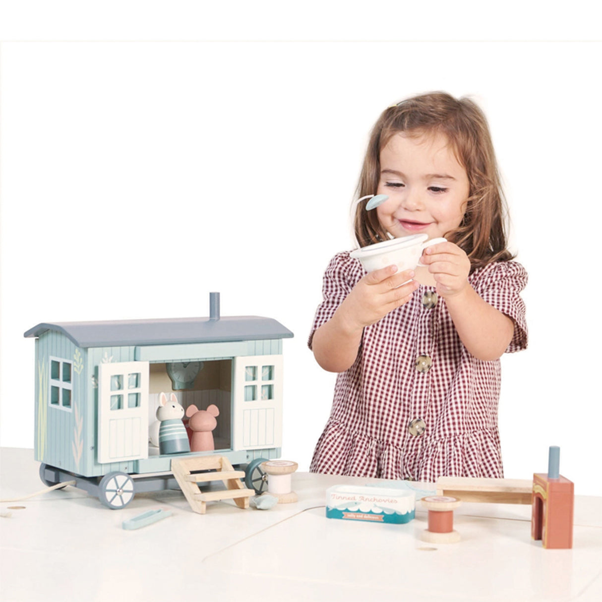 Child playing with a toy Shepherd Hut and accessories on a white background