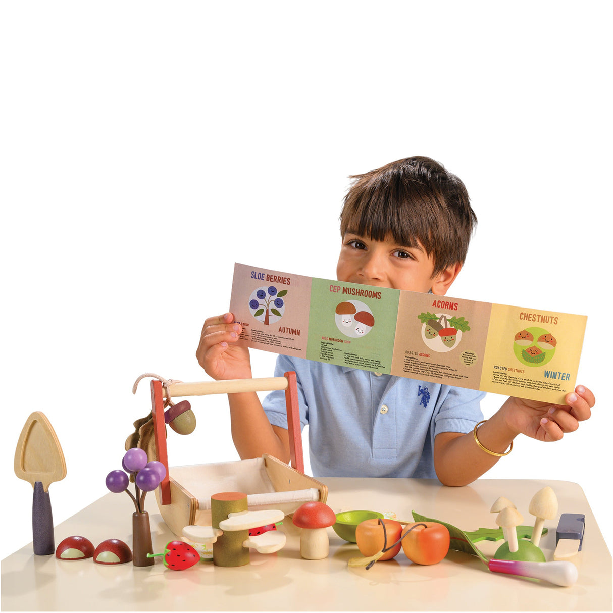 Child holding a educational leaflet with a wooden play set Wild Wood Foraging Trug