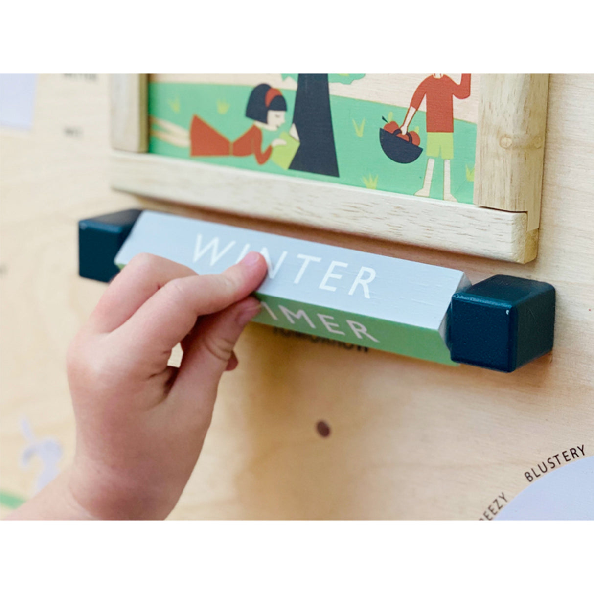 Hand holding a 'Winter Timer' device with a wooden frame and colorful artwork in the background.