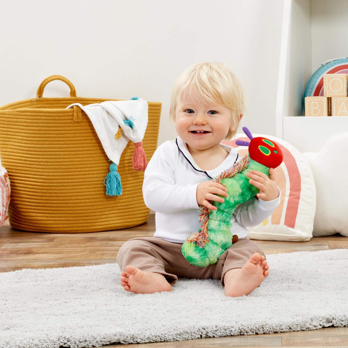 Child playing with a very hungry caterpillar toy in a room with a yellow basket and colourful decorations.