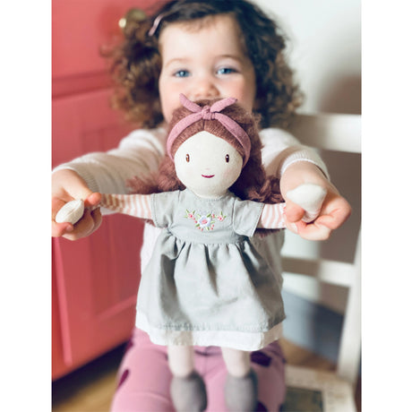 Child holding a small rag doll with a gray dress and pink headband.