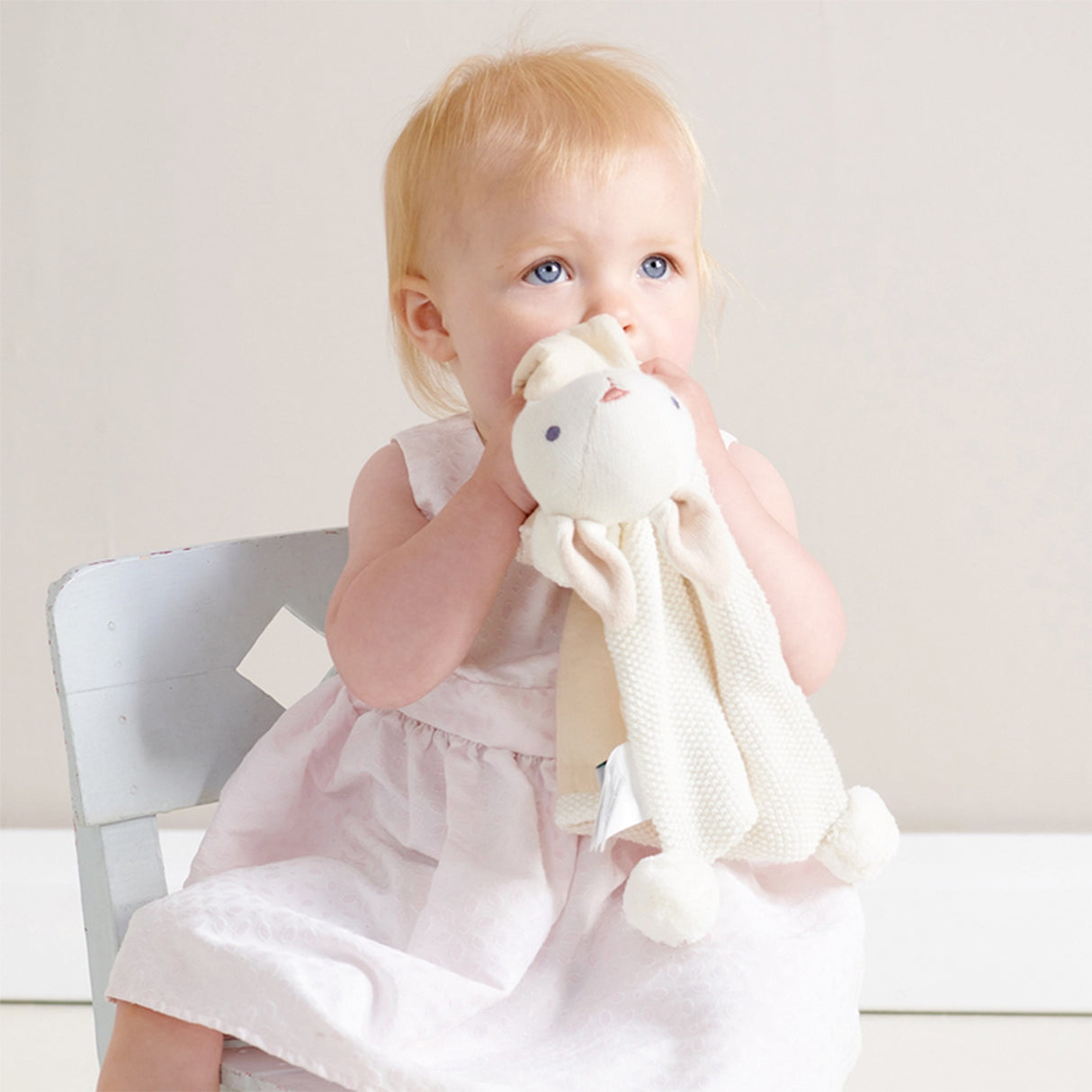 Child holding a plush bunny soother toy in a softly lit room