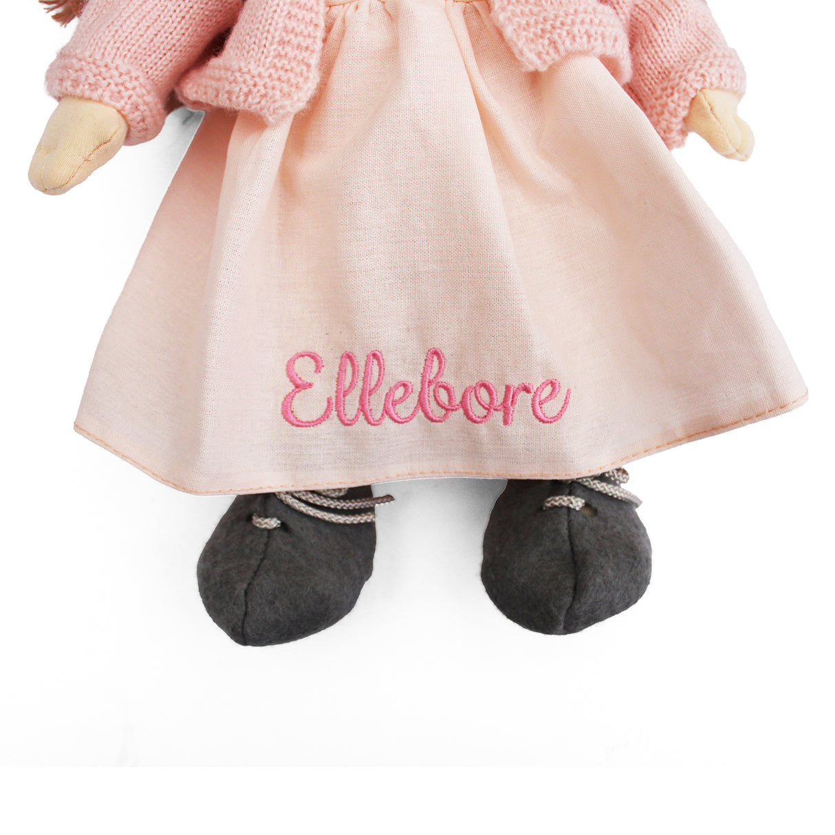Doll with pink dress and 'Ellebore' embroidery on a white background