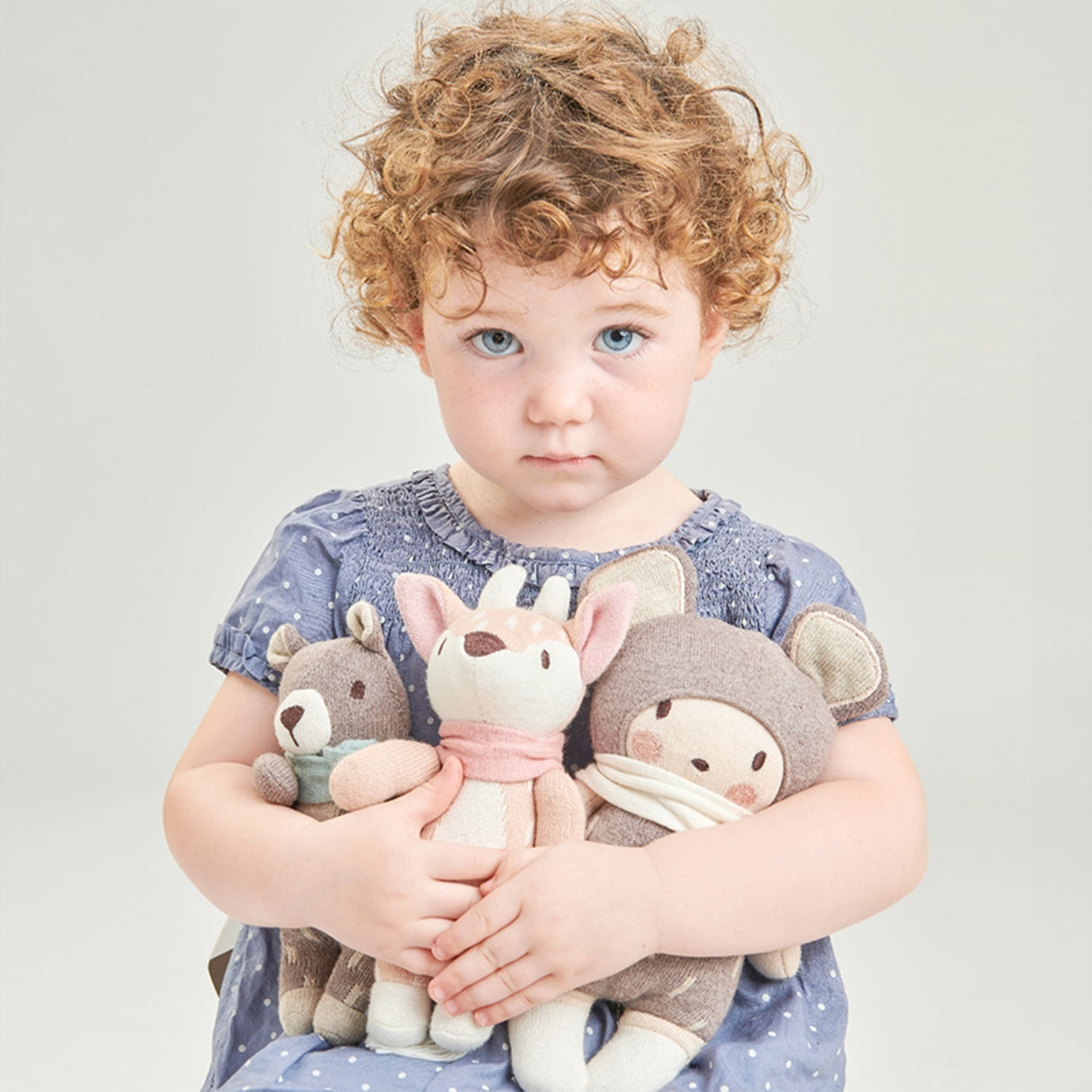 Child holding three stuffed animals against a plain background