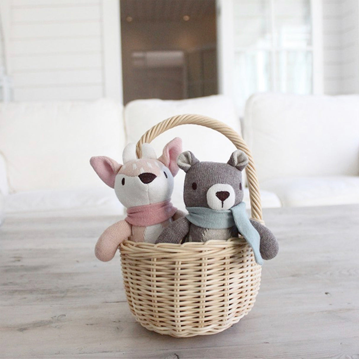 Two plush toys, a fox and a bear, in a wicker basket on a light wooden floor.
