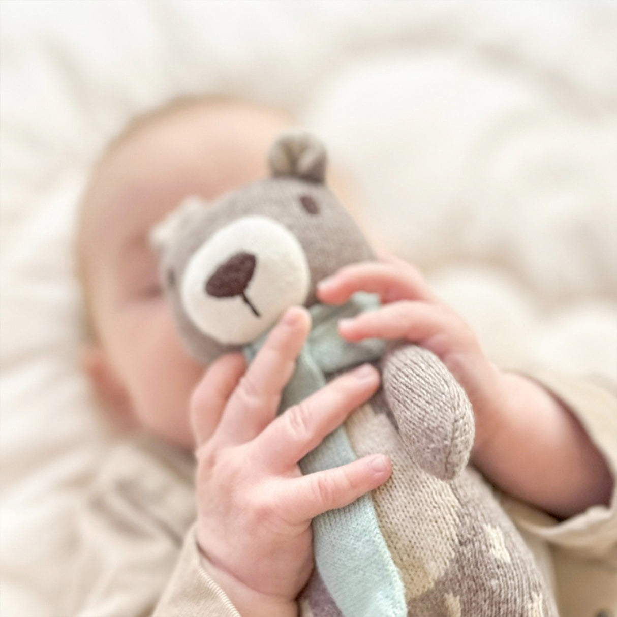 Baby holding a Knitted teddy bear with a light blue scarf with a blurred background