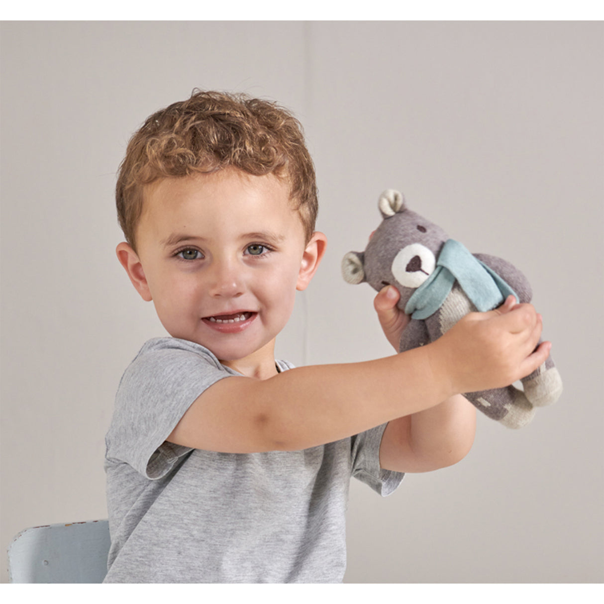 Child holding a Knitted teddy bear with a light blue scarf against a plain background