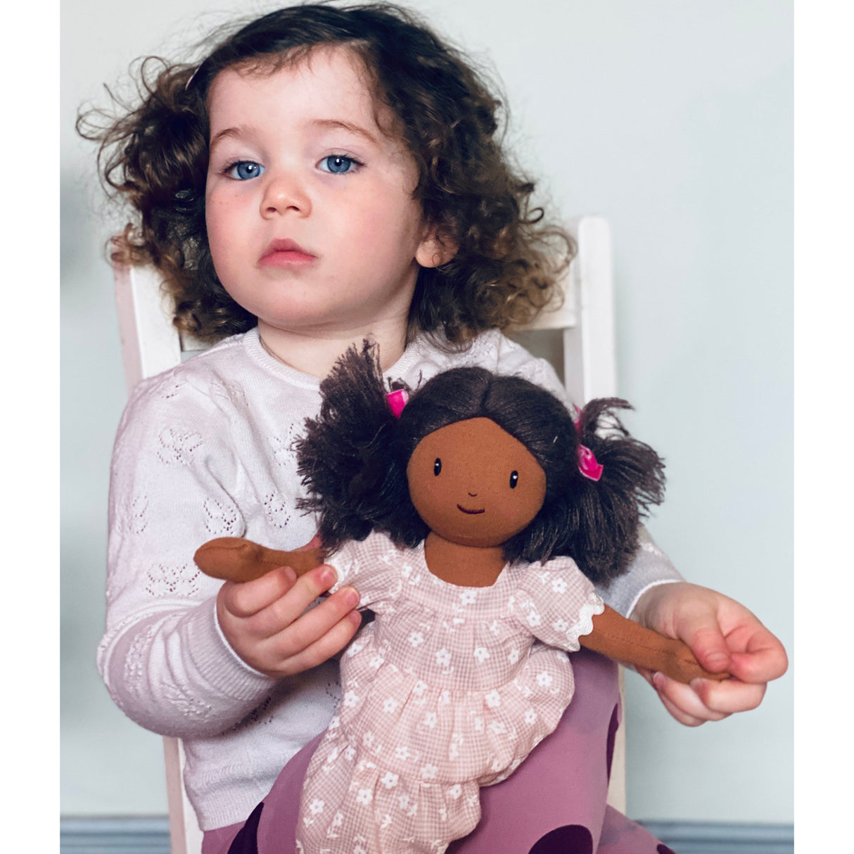 Child holding a doll with dark hair and a pink dress