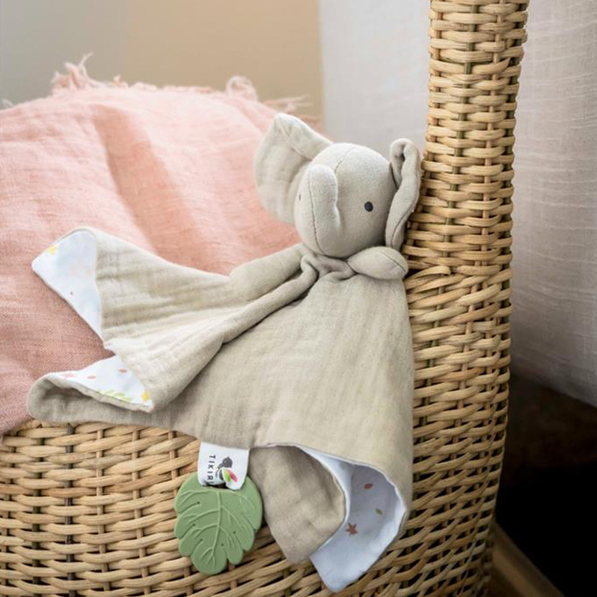 Baby muslin comforter with attached elephant and green leaf teether on a wicker basket