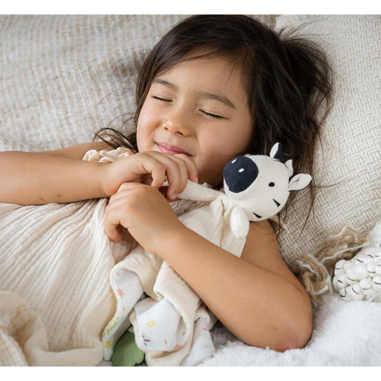 Child cuddling a muslin comforter with an attached zebra toy and green leaf teether
