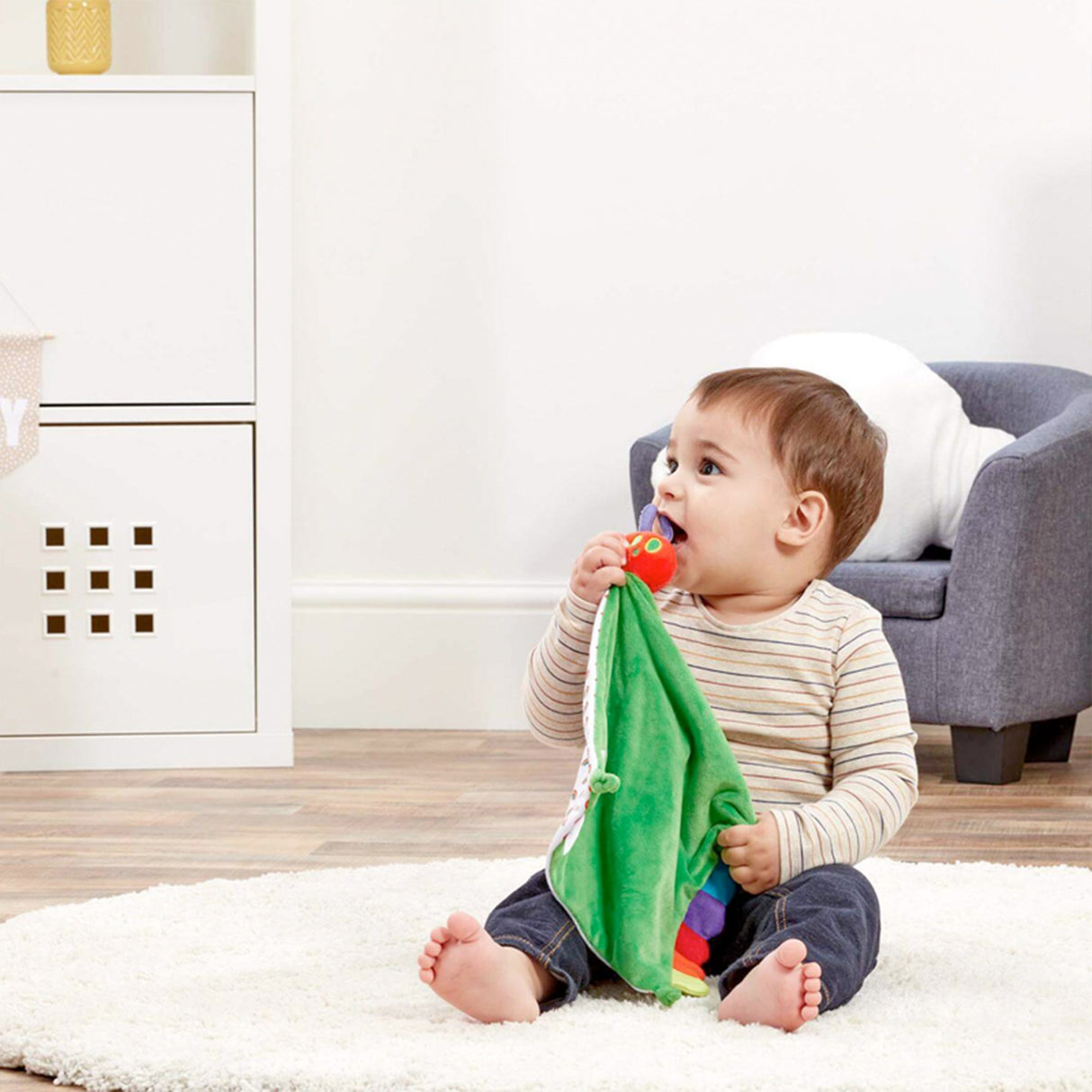 Child playing with The Very Hungry caterpillar Green comfort blanket with colorful rainbow edges and tags in a home setting