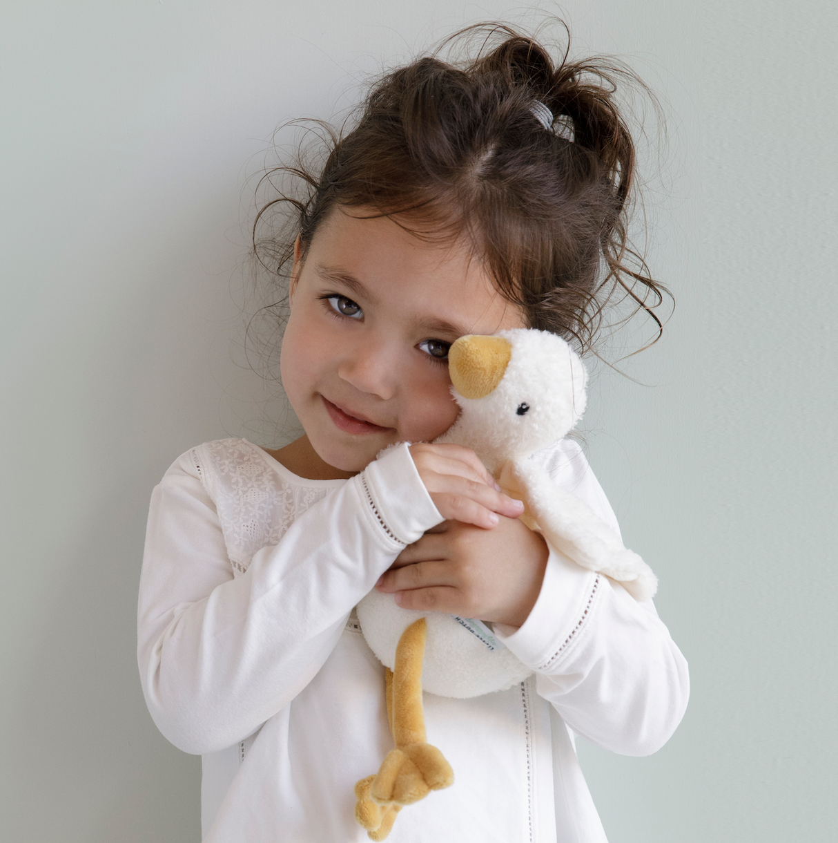 A little girl hugging a soft cuddly goose soft toy with a cream body and wings and a orange beak and feet.