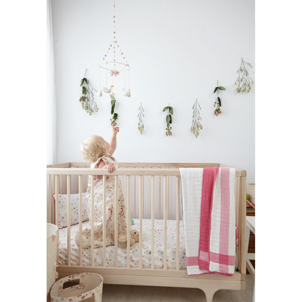 Petit Pehr mobile has five swans hanging above and a pink lily in the centre over a baby cot