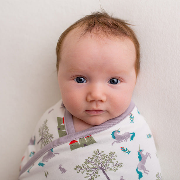 A baby wrapped in a Pigeon Organics Fairytale Unicorn Blanket