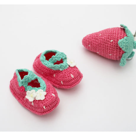 Pair of pink strawberry crochet baby shoes with green straps and white flowers on a light background