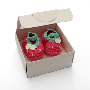 Pair of pink crochet Strawberry baby booties with green tops and white flowers in a box on a white background