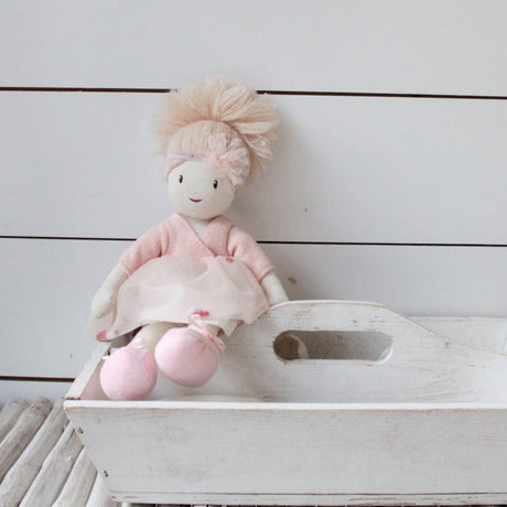 Stuffed rag doll with pink outfit and blonde hair on a white wooden surface