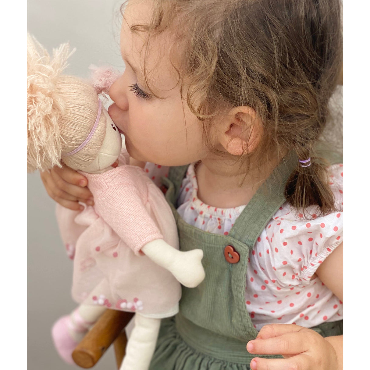 Child kissing a rag doll with a neutral background