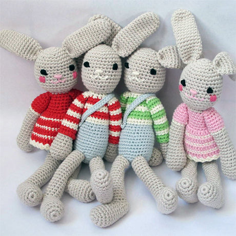 Four organic crochet bunny soft toys by Attic Textiles in red, blue, green and pink outfits on a white background