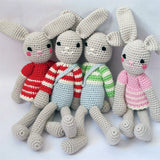 Four organic crochet bunny soft toys by Attic Textiles in red, blue, green and pink outfits on a white background
