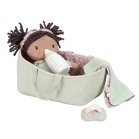 Little Dutch Baby Doll Evi lying in sage green travel basket holding a bottle, with dummy beside basket, on white background