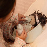 Child feeding Little Dutch Baby Doll Evi a bottle while doll lies in sage green basket