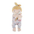 A soft baby doll with blonde hair, wearing a blue, pink, and white floral jumpsuit and holding a small white plush goose and bottle.