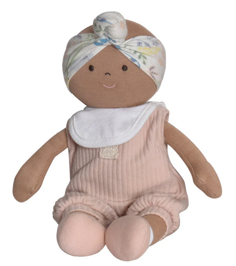 A soft pink cloth baby doll with a floral headband and a removable white bib, sitting with a flowing headscarf.