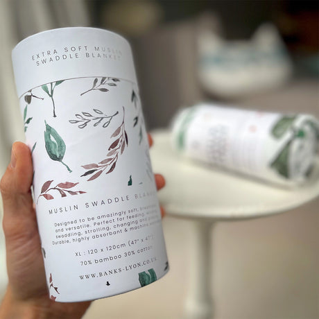 Person holding a cylindrical product packaging with leaf design and text.
