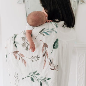 Woman holding a baby wrapped in a botanical blanket against a white background