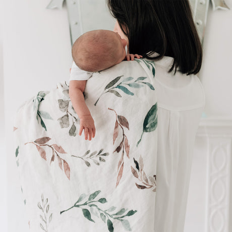 Woman holding a baby wrapped in a botanical blanket against a white background
