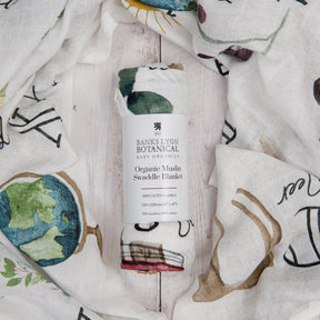 Banks Lyon Botanical Organic Muslin Swaddle Blanket with artistic designs on a wooden surface.