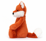 A plush toy depicting a fox cub with fluffy white ears, feet, and tail-tip, sitting with a reddish-brown body.