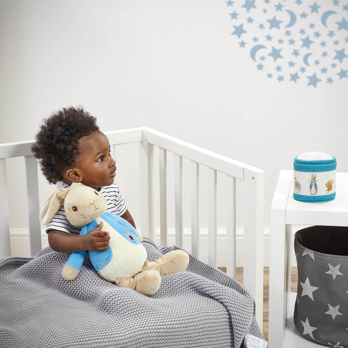 baby in bed with Peter Rabbit soft toy and a musical night light showing lights on wall