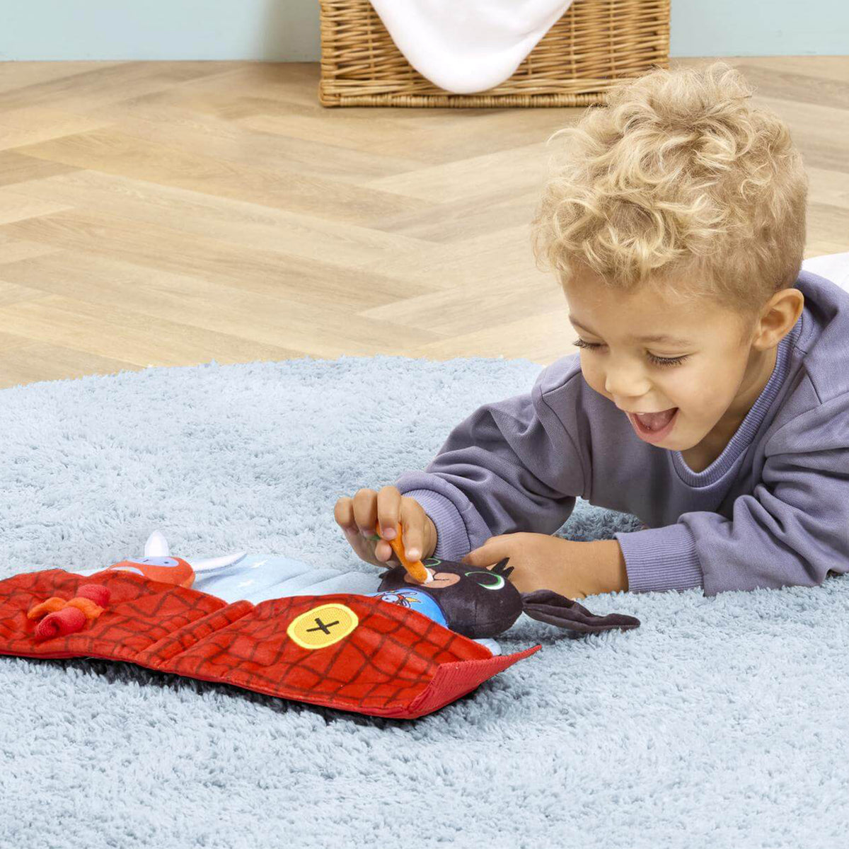 A young child lies on a rug, playing with a bing soft toy 
