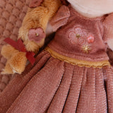 Close-up of a floral embroidery design on a dolls pink dress on a textured fabric background.