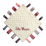 Baby comfort blanket with textured surface and colorful ribbons around the edge, featuring the name 'Ida Maeve'.