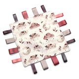 Handmade baby taggy comforter with a floral pattern on a white background, backed with plush fabric, and secured with ribbon tags.