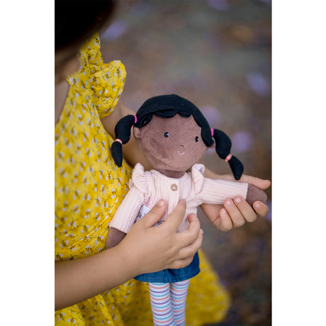 GIrl holding a rag doll with dark hair styled in pigtails, wearing a pink top and striped pants.