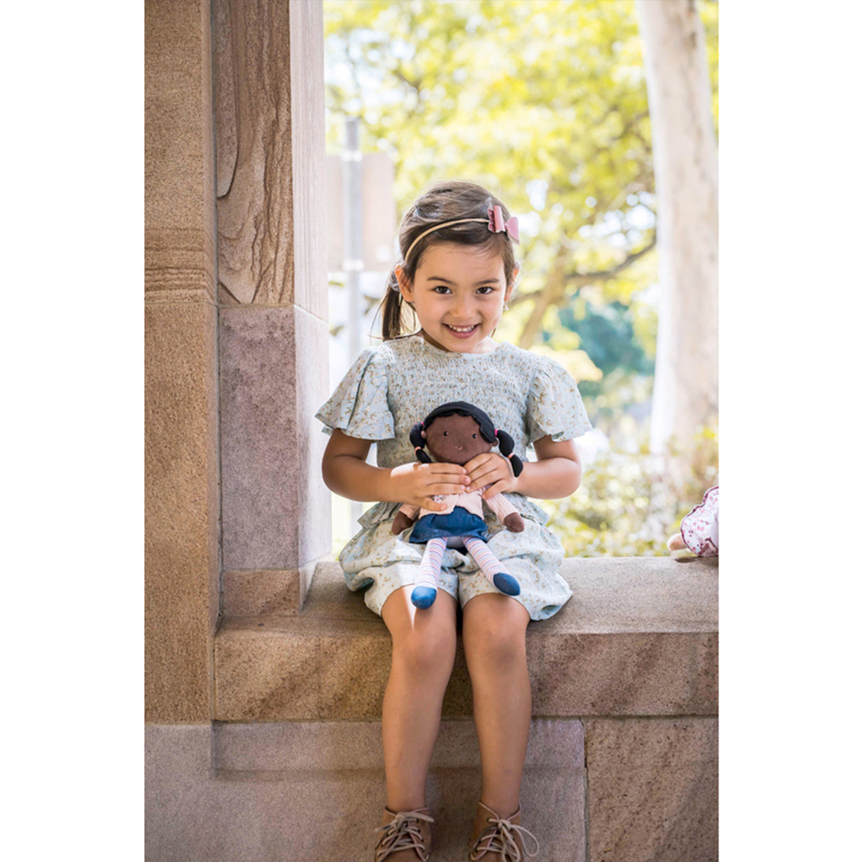 Young girl holding a doll with a blurred outdoor background