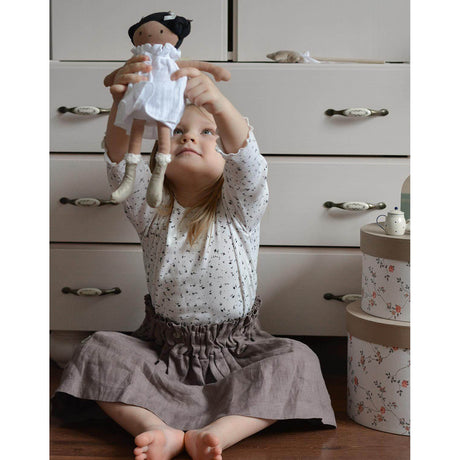 Child holding a doll in front of a white dresser with floral boxes.