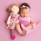 Newborn baby lying with a rag doll with pink floral dress on a pink background