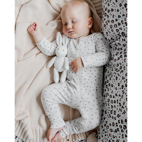 Baby in a star polka dot bodysuit holding a soft white bunny toy, lying on a soft surface with leopard print fabric.