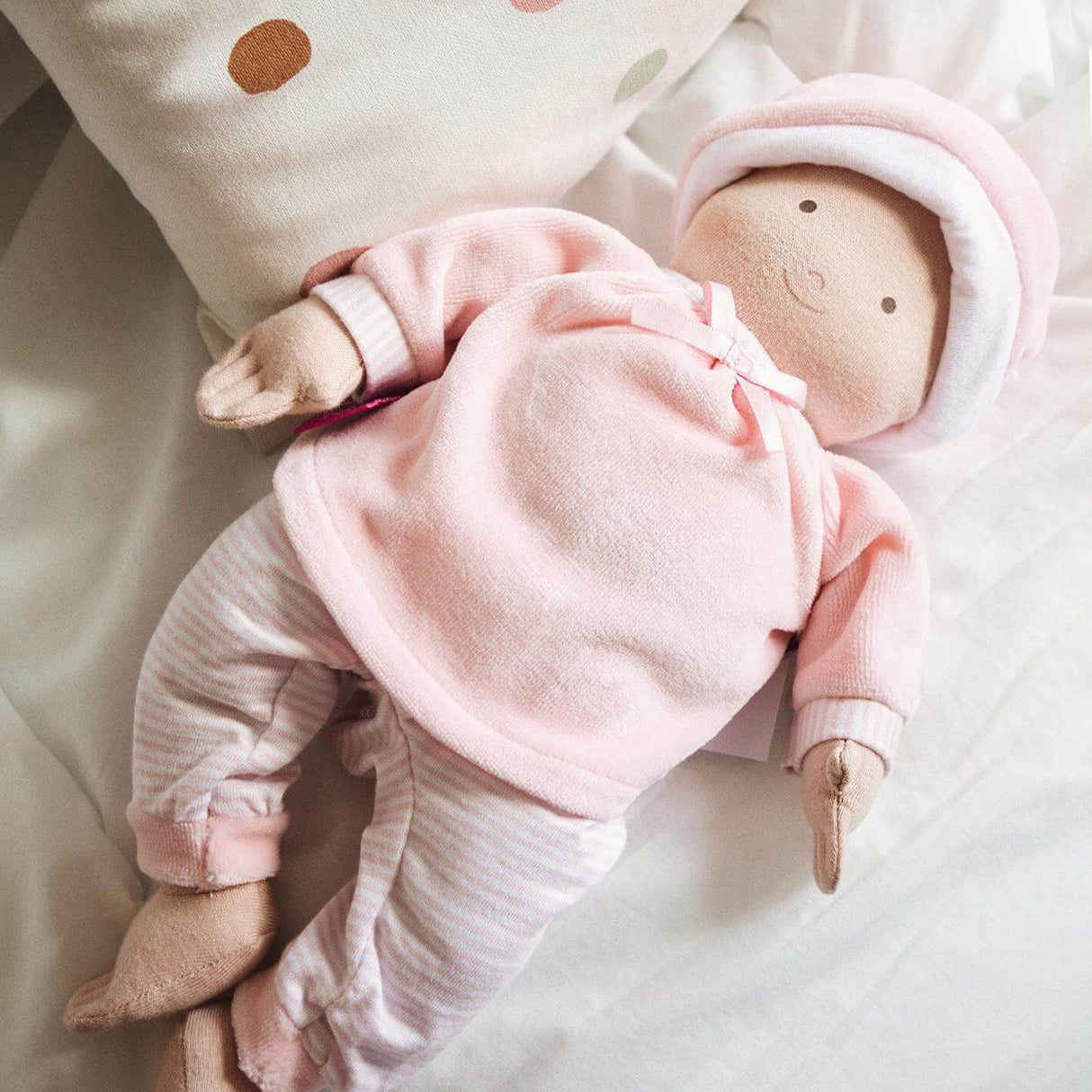 Baby doll in pink outfit on a soft surface