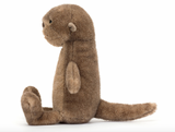 A plush toy depicting a brown otter with a soft, mottled fudge fur texture, butterscotch ears, a black nose, and bright black eyes. It is seated with a long, chunky tail extended.