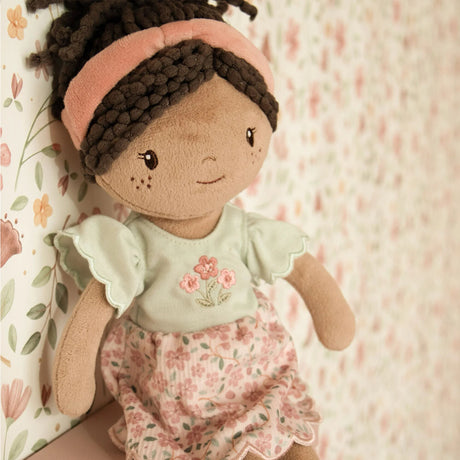 Soft doll with floral pink and sage green dress, pink headband and curly brown hair tied in a ponytail.