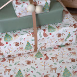 Woodland-themed gift wrap with deer, trees, and other elements on a white background.