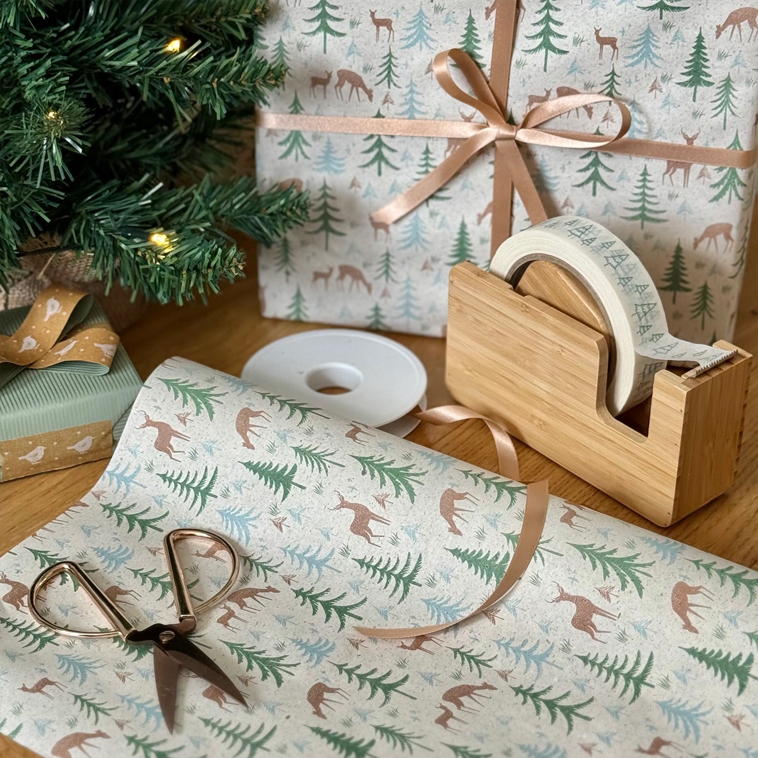 Gift wrapping paper with forest design, scissors, tape, and a Christmas tree.