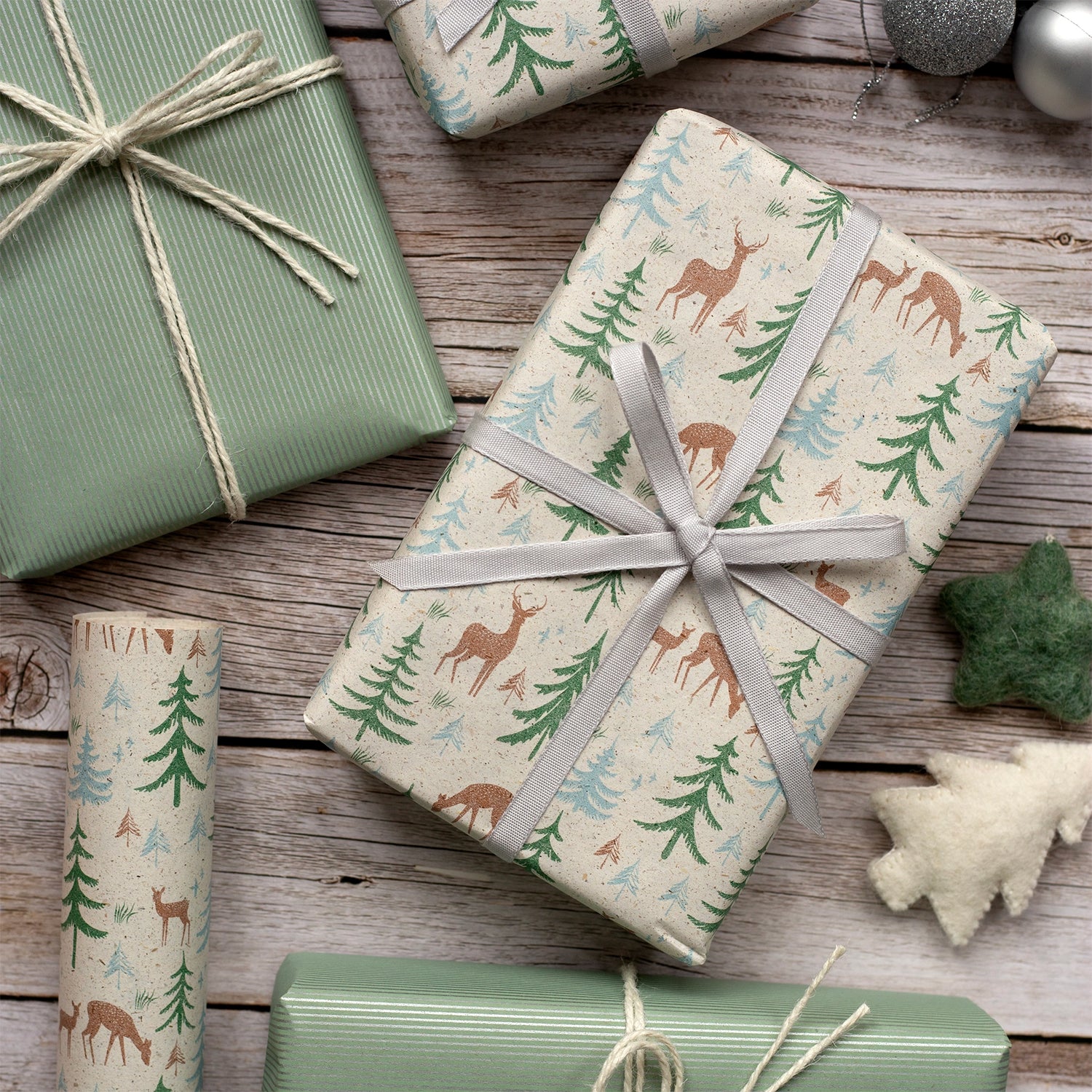 Gifts wrapped in festive paper with deer and tree patterns on a wooden surface.