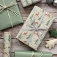 Gifts wrapped in festive paper with deer and tree patterns on a wooden surface.